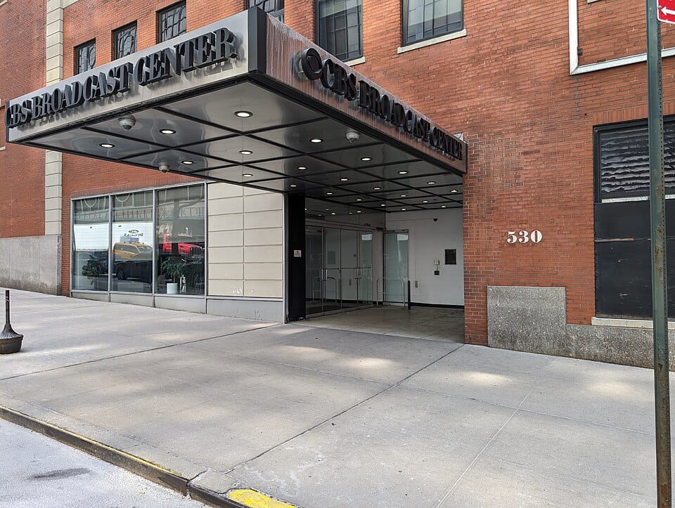 Exterior of the CBS Broadcast Center in NYC; an imposing, industrial brick building with a dark metal canopy.